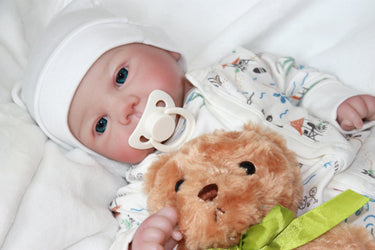 A baby doll lies on a bed next to a teddy bear, evoking a sense of childhood comfort and companionship.